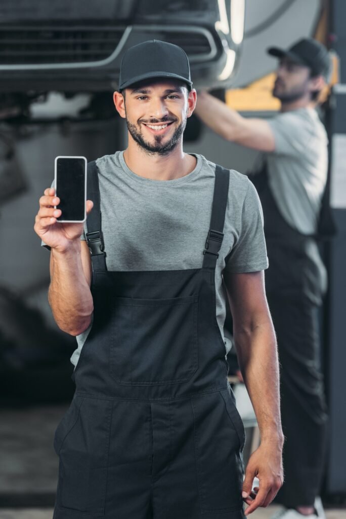professional mechanic showing smartphone with blank screen, while colleague working in workshop